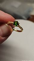 Close-up photo of a gold electroplated sterling silver ring featuring a vibrant green round chrome diopside center stone and clear cubic zirconia stones on band.