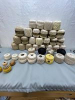 Full view of multiple large balls of crochet thread in ecru and a few smaller balls of other colors on a flat surface