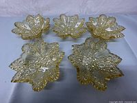 Top view of all five amber Fenton glass kerchief trinket bowls showing daisy button floral and geometric pattern and ruffled sawtooth edges.