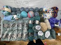 Lot overview showing all yarn rolls and skeins arranged in multiple rows on a fabric surface.
