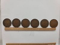 Photo showing six Canadian large one cent coins from 1915 to 1920 aligned horizontally with a white background and a strip of paper beneath them.