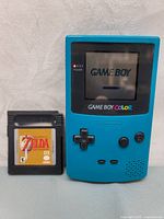 Teal Game Boy Color front powered on showing startup screen with Zelda game cartridge placed beside console