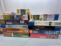 Photo of boxed puzzles stacked in two rows, showing box art and piece counts including 1000-piece, 1500-piece puzzles.