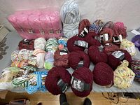 Wide view of assorted wool yarn rolls and unopened pink yarn pack on table
