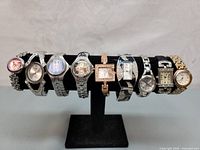 Photo of 9 wrist watches displayed on a black watch stand showing a variety of metal bands and watch faces.