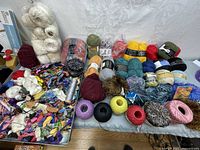 Overview of large assortment of yarn balls and skeins in many colors with various textures, plus many small spools and skeins of embroidery thread and trimmings spread out on table