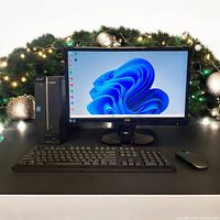 Front view of Acer Aspire desktop, AOC monitor showing Windows 11 Pro, with keyboard and mouse on display table decorated with holiday lights.