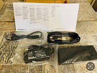 All contents laid out on tiled surface including power supply adapter, power and data cables, and printed manuals.