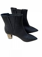 Side view of both ankle boots showing black faux leather and distinct metallic heels.