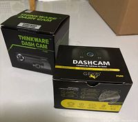 Two boxed dash cams on a white surface: Thinkware F200 and Geko P500.