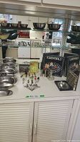 Shelf with multiple metal mixing and serving bowls, glass egg plate, colorful handled utensils, and boxed serving sets.