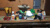 Wide view showing the entire table with multiple items including boots, vice, automotive bottles, and other household items.
