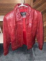 Front view of red leather biker jacket on hanger showing zipper and collar details.