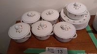 Full set of six white china soup bowls with lids and side plates arranged on table