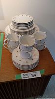 Photo showing stacked plates with cups and saucers on a table, revealing the delicate gold pattern on white china.
