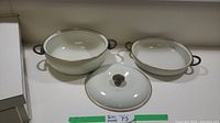 Two white enamel cookware pieces and one lid set on table