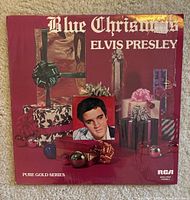Close-up of Elvis Presley Blue Christmas vinyl record cover with red background, presents, and photo of Elvis Presley, marked Pure Gold Series by RCA.