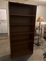 Front view of the tall wooden bookcase showing five shelves and dark brown finish.