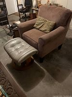 Brown corduroy armchair with cushion and white leather tufted ottoman placed on concrete floor.