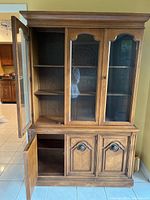 Front view of the wood china cabinet showing three glass panel doors open on upper display section and two wood paneled doors open on lower storage section.