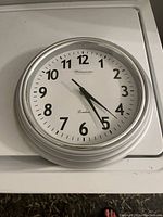 White round wall clock with black numbers and black hands reading around 4:26. Brand name 'Westminster London' visible on clock face.