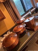 Photo of three hammered copper covered pots of different sizes on a kitchen counter near a sink.