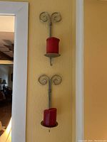Two metal wall-mounted candle holders holding red pillar candles with decorative curled tops.