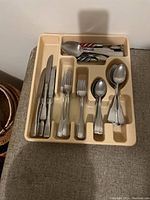 Beige plastic flatware organizer tray containing stainless steel knives, forks, and spoons in separate compartments.