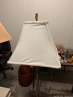 Close-up of white fabric trapezoidal lamp shade with brass finial on top.