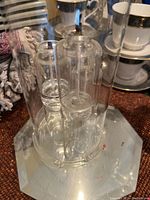 Close-up of three clear glass oil candles with wicks inside a transparent cylindrical enclosure on metallic base.