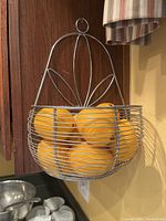 Metal wire hanging basket filled with six large yellow faux lemons hung on wooden wall.