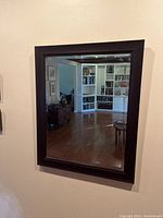 Full view of a rectangular mirror with a dark wood frame hanging on a wall reflecting a living room.