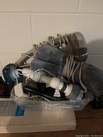 Plastic container filled with multiple different electric massagers and cords, showing variety of types in lot.