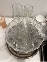 Clear large crystal bowl with cut diamond pattern and pedestal base with small tumblers inside and two taller glasses behind.