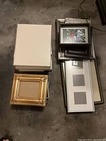 Overview of the collection including a decorative gold ornate frame, plain white frames stacked, and various other frames in black and metallic finishes.