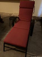 Full view of the outdoor lounge chair with red cushions, showing the black metal frame and padded sections.