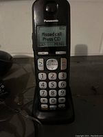 Front view of one Panasonic cordless telephone handset on a charging base, showing the LCD screen with 'Missed call Press CID' message and numeric keypad.