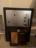 Large black framed magnetic dry erase board with several magnets and a dry erase marker, resting against a wall and floor.