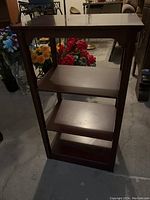 Full view of wooden shelf with three shelves and a flat top, medium brown finish, standing on a concrete floor.