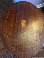 Close-up of the oval top surface of the side table showing inlaid wood design with a central sunburst pattern.