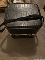 Black textured carry case with a shoulder strap, closed and locked, showing exterior condition.