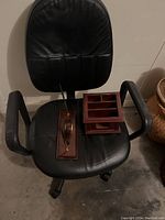Black leather office chair with armrests and wheels with wooden desk organizer and pen holder set on the seat