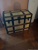 Front view of antique dome-top wooden trunk with cream panels and dark metal bands.