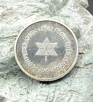 Front side of the commemorative token showing triangular maple leaf pattern and confederation dates.