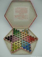 Open hexagonal star-shaped game board with colored marbles arranged on playing points showing vintage condition.
