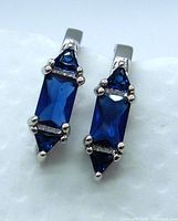 Close-up photo of earrings showing blue lab sapphire stones and silver prong settings.