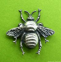 Top view of silver tone honey bee brooch showing detailed wings, body texture, and antennae on bright green background.