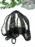 Five black peacock freshwater rice pearl necklaces arranged on a rock, showing multiple strands with glossy black iridescent pearls.