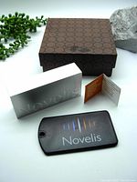 Aluminum brick, access tag, info card, and presentation box lid placed on table with green plant and rock on side for display.