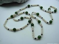 Necklace laid out showing alternating pattern of white pearls, green jade beads, and small black spacer beads.
